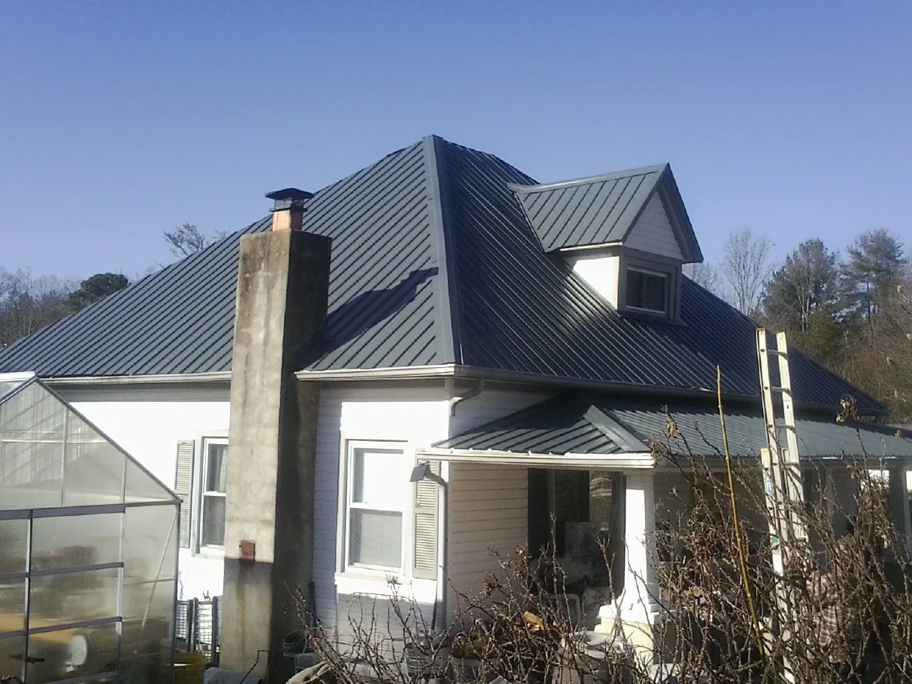 Dark blue standing seam metal roof on a white farmhouse with dormer — Slate & Tile Roof Repair by Roofing Brothers in Zirconia