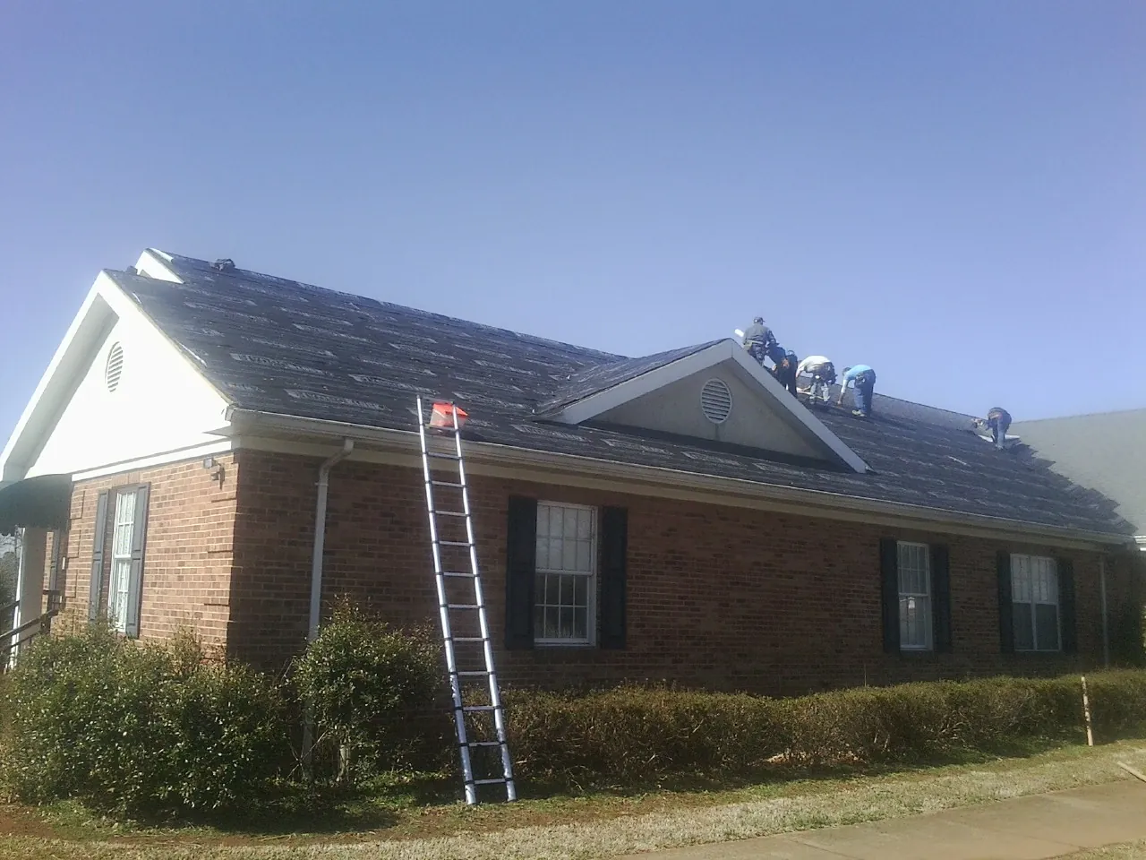 Crew tearing shingles off a brick ranch roof with a ladder set — Emergency Roof Repair work by our crew in Zirconia