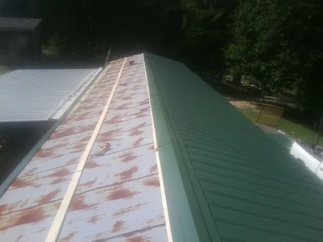 Old rusted panels beside newly installed green metal roofing — Wind Damage Roof Repair by Roofing Brothers in Zirconia