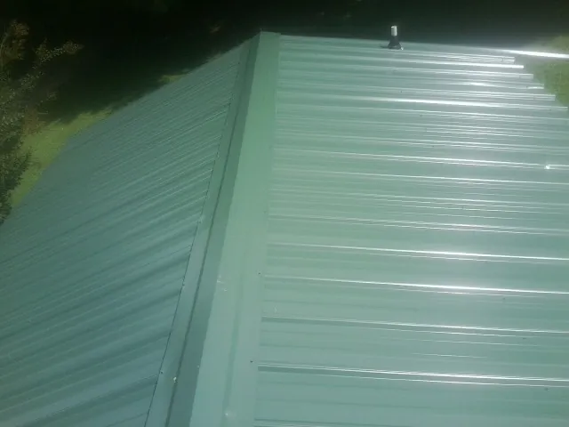New green metal panels meeting at the ridge of a roof — Flat Roof Repair work by our crew in Zirconia
