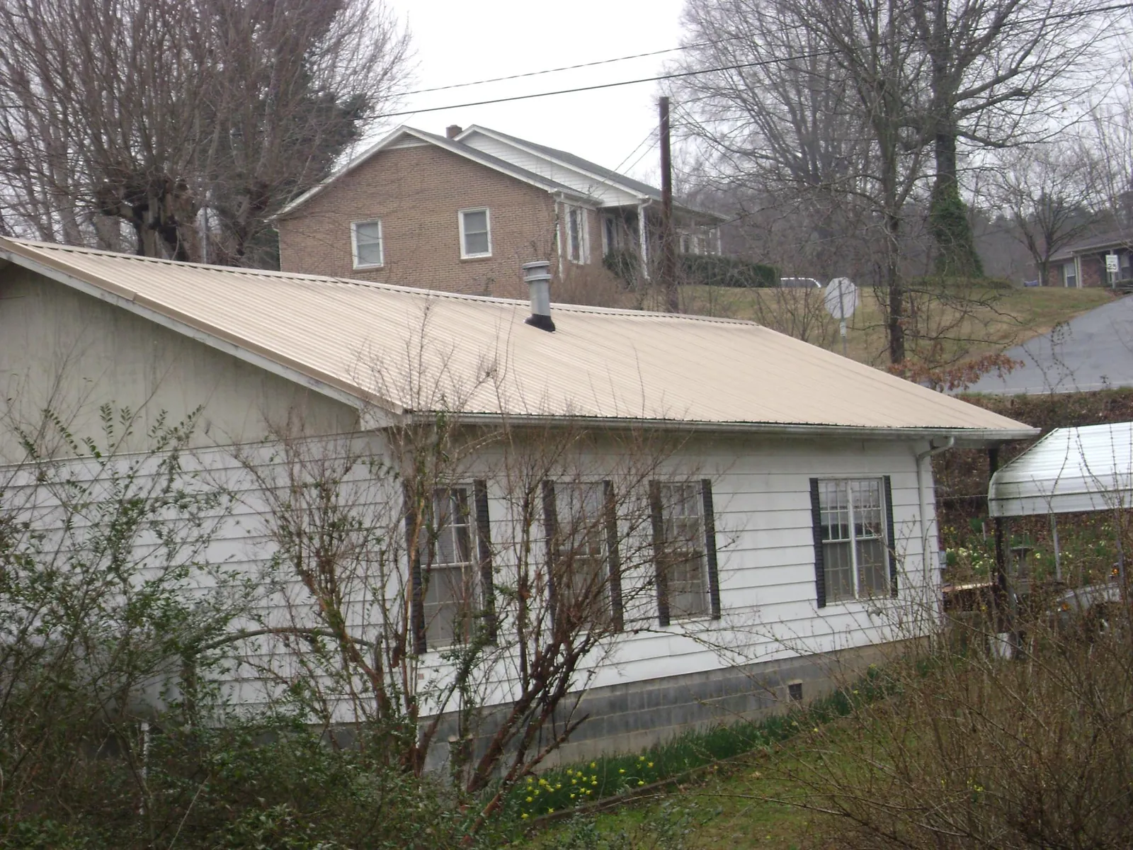 Tan metal roof on a white sided house set into a hillside — Commercial Roofing by Roofing Brothers in Zirconia